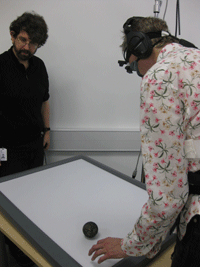 Andy Clark (right) tracking a ball sent rolling towards him by Simon Holland (left) using a vibrotactile corset driven by a head-mounted camera (November 2008). Photo by Jon Bird.